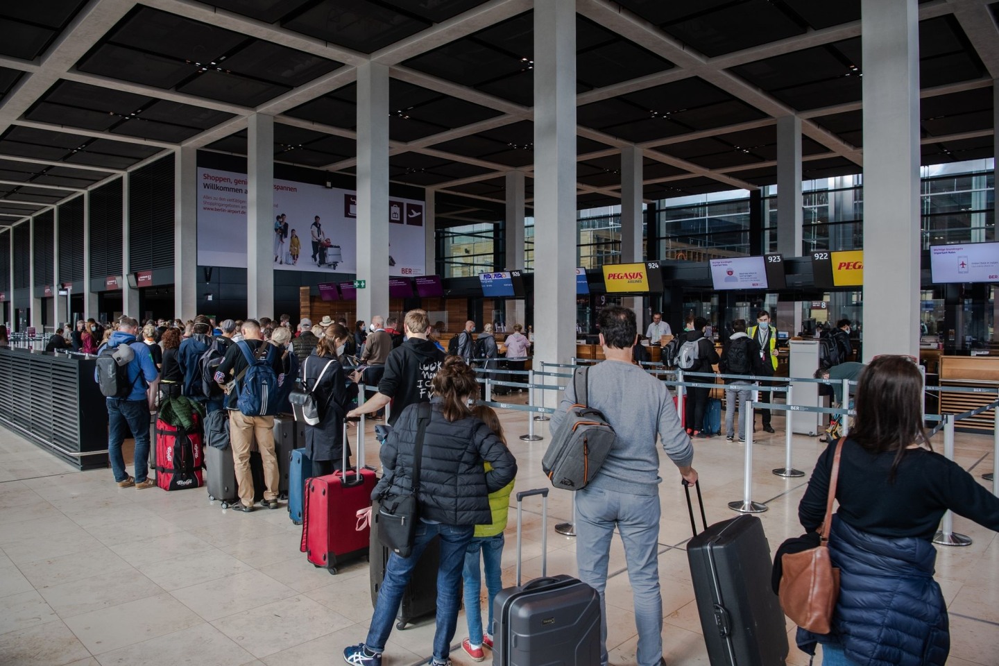 Reisende stehen am Flughafen BER vor einem Check-in-Schalter. Corona-Regeln beschränken weiterhin das freie Reisen.